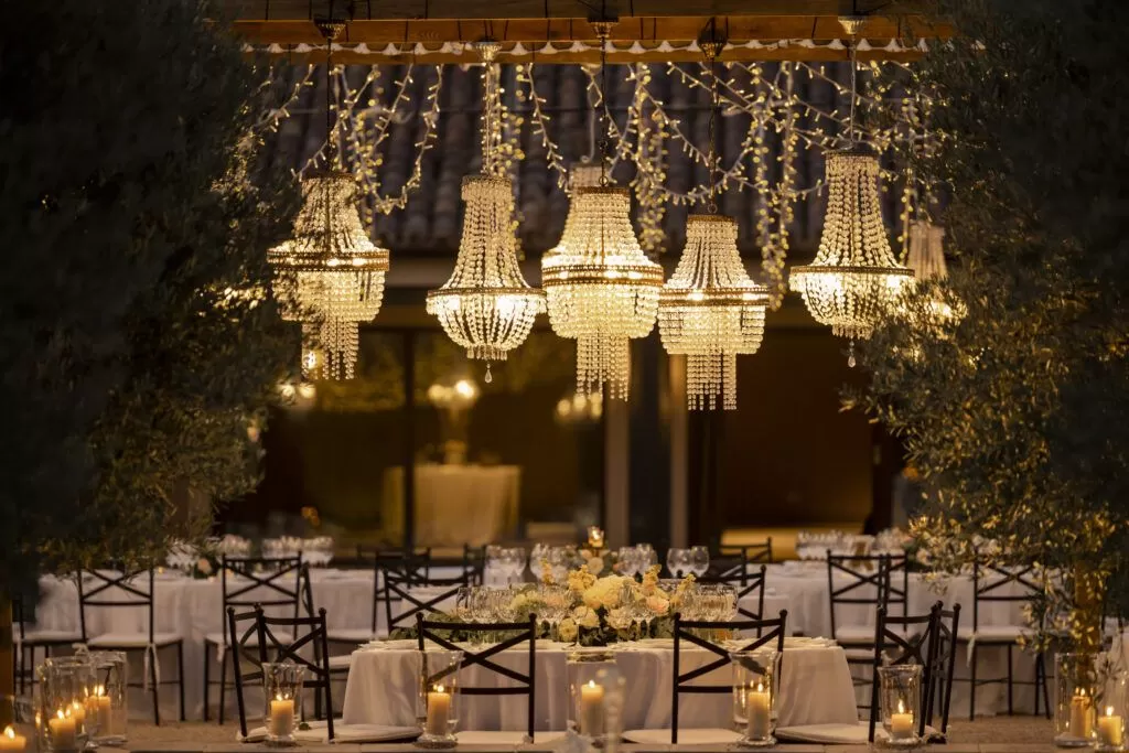 zona de banquete al aire libre con montaje de lamparas de araña chandeliers e iluminacion micro led tipo dairy o hadas