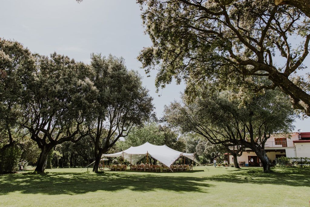 Interior de carpa beduina de color blanco con mastiles de madera con mesas de banquete montadas y sillas de bambu.