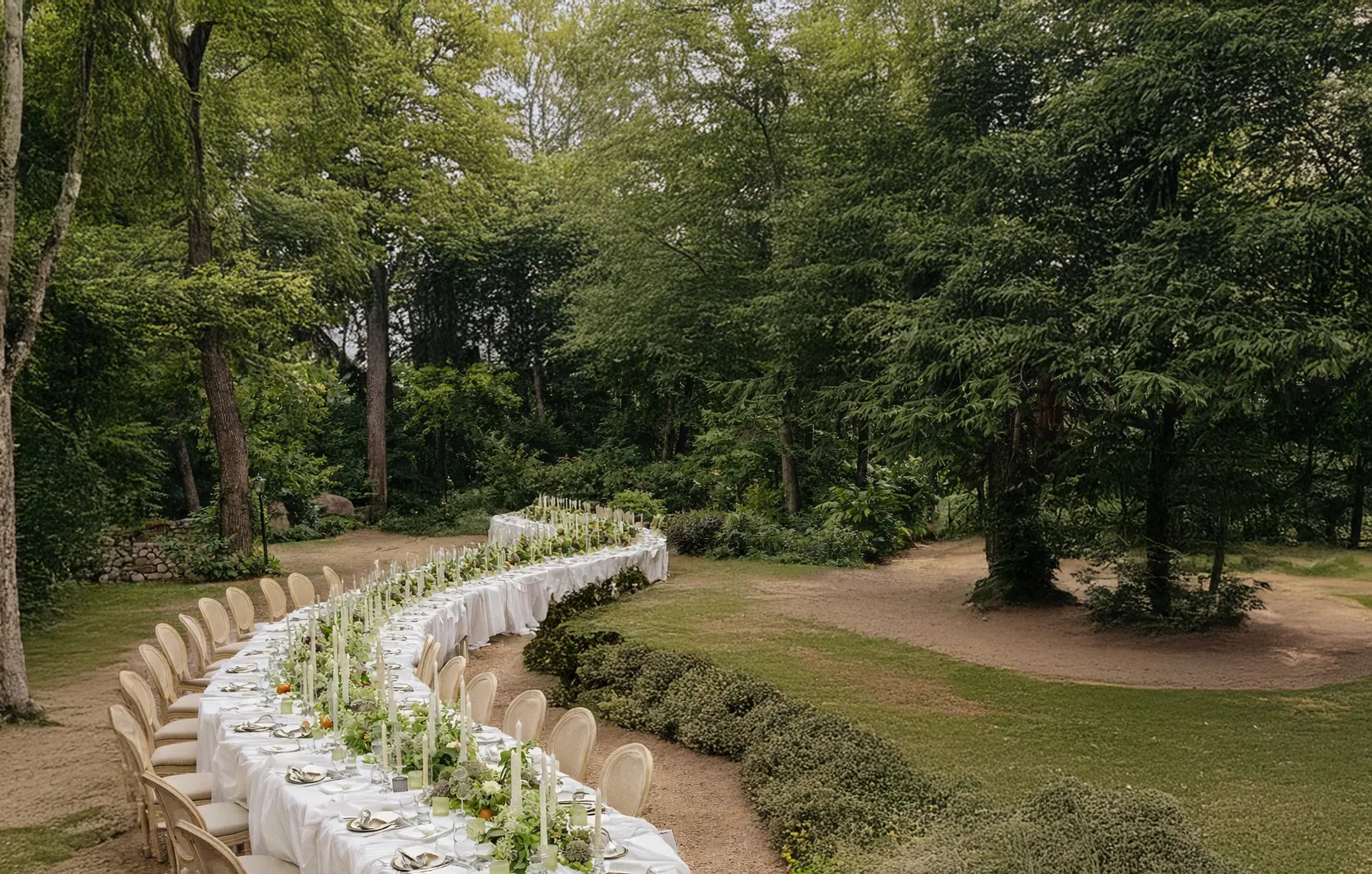 Primer plano de mesa serpenteante para boda con mantel blanco drapeado y montaje de copas de cristal.