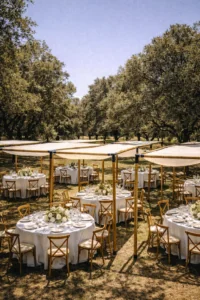 Varias mesas redondas con manteles blancos y centros de flores, dispuestas bajo módulos individuales de pérgolas rústicas de madera en un bosque o jardín con árboles.