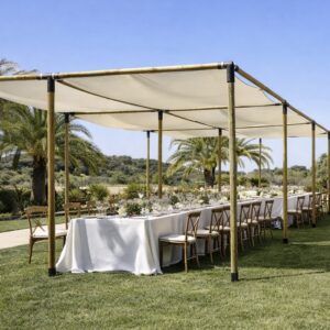 Estructura de pérgola de madera con toldo de lona blanca tensada cubriendo una mesa imperial con mantelería blanca y sillas Crossback en un jardín con palmeras.